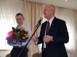 Pan Paweł Guz i Pan Tomasz Futera składający życzenia i wręczający upominki aparat fotograficzny i kwiaty